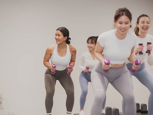 A group of people squat and do tricep exercises with hand weights at So Fitness. 