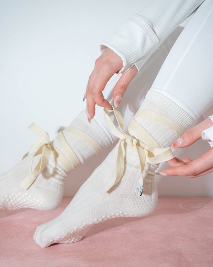 A pilates student ties a bow on her white high top balletcore grip socks. 