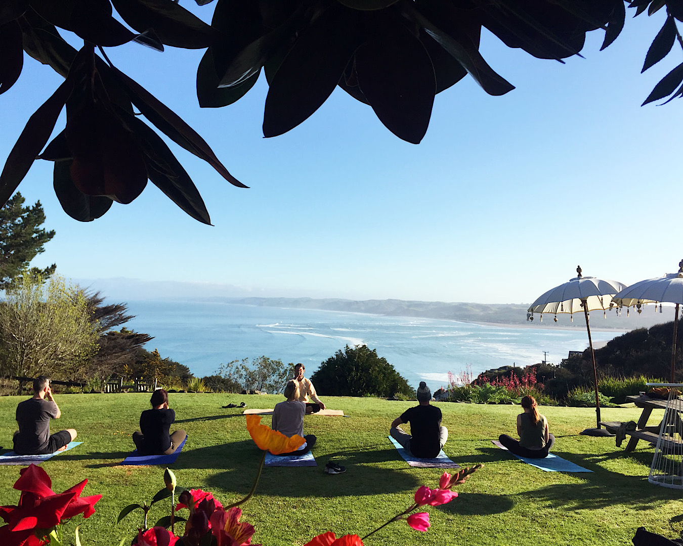 A small group of yogis enjoy a morning vinyasa with a beautiful view of Whale Bay in Raglan, at Solscape, one of the best retreats in New Zealand. 