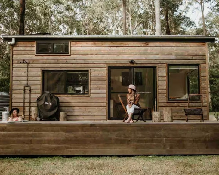 A woman sits on the deck while another woman lies in the outdoor bath at Soul Wood romantic Airbnb in NSW