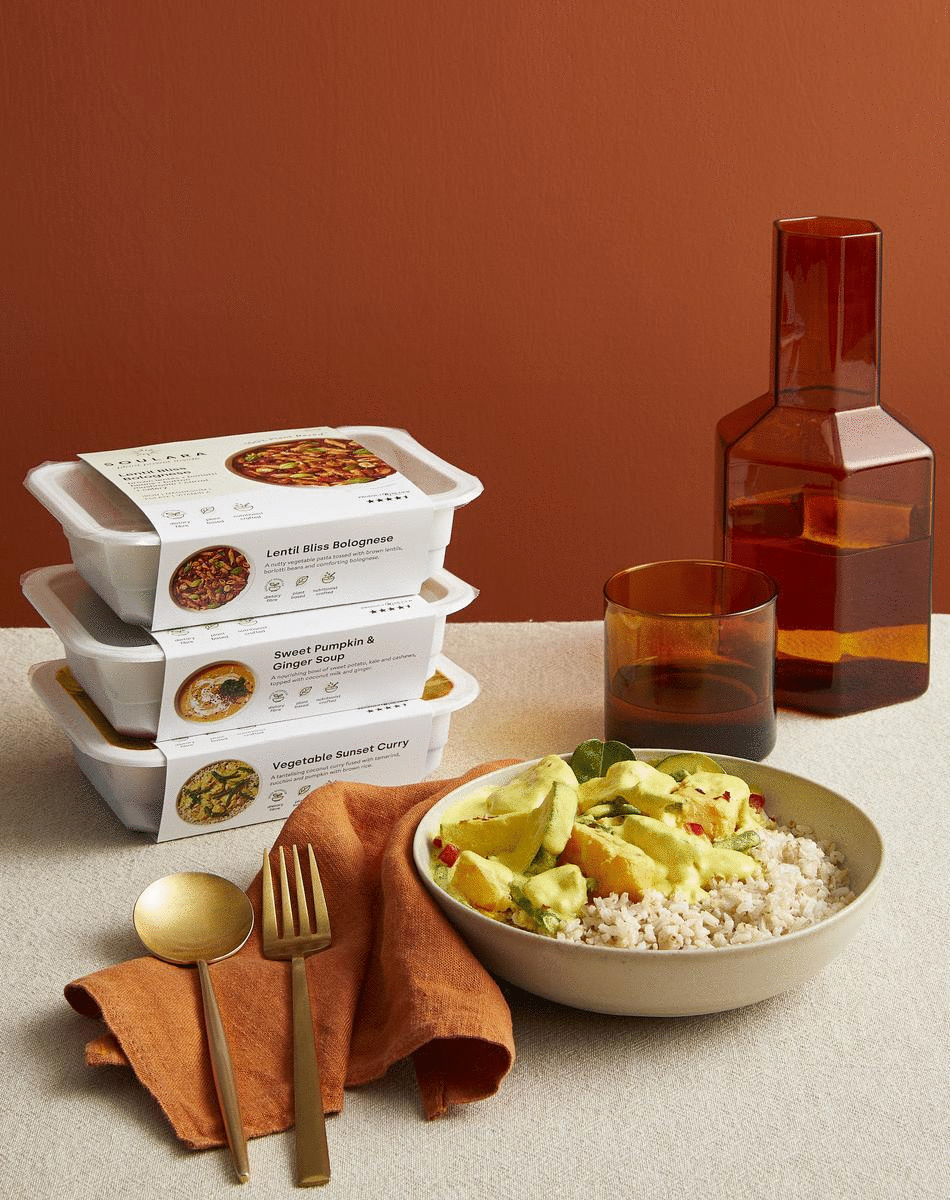 Stacks of premade plant based meals sit next to beautiful glassware.
