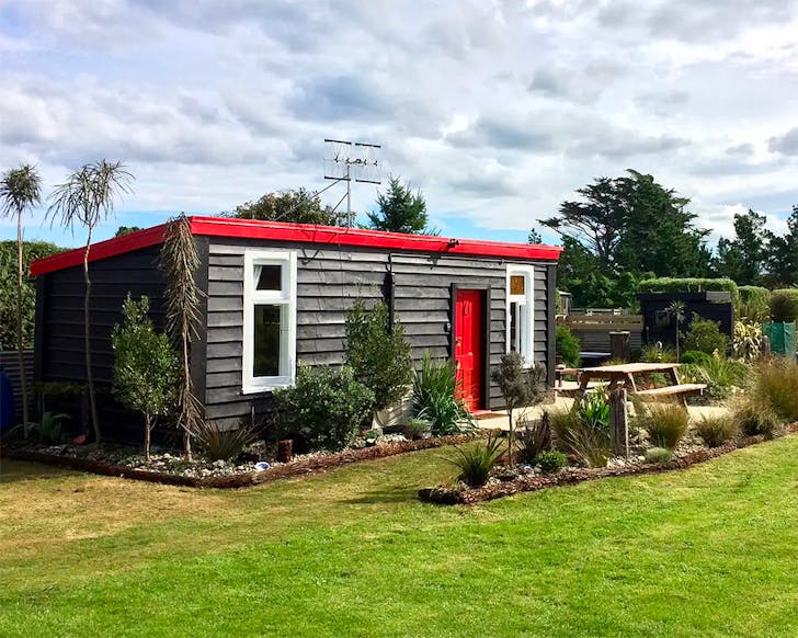 A red and black bach in farmland is seen from the outside.