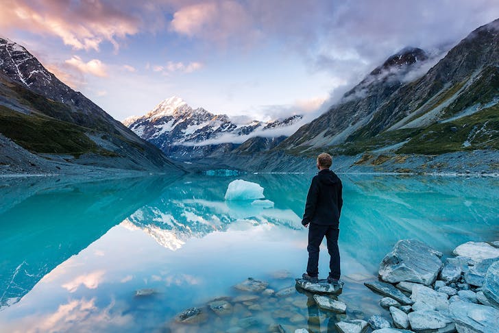 A hiker looking at Mt Cook from lake with iceberg, New Zealand
