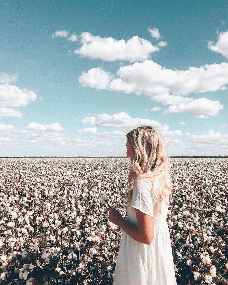 A woman smiles and looks at a cotton field.