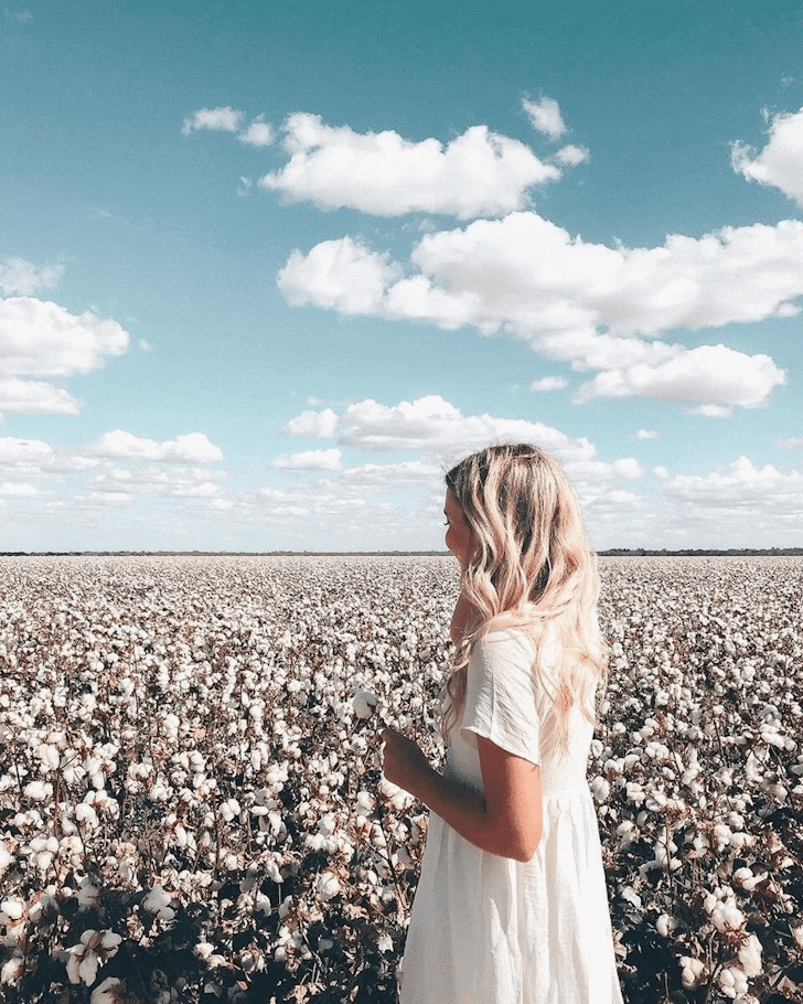 A woman smiles and looks at a cotton field.
