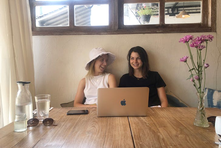 Two woman sit at a cafe table with a laptop