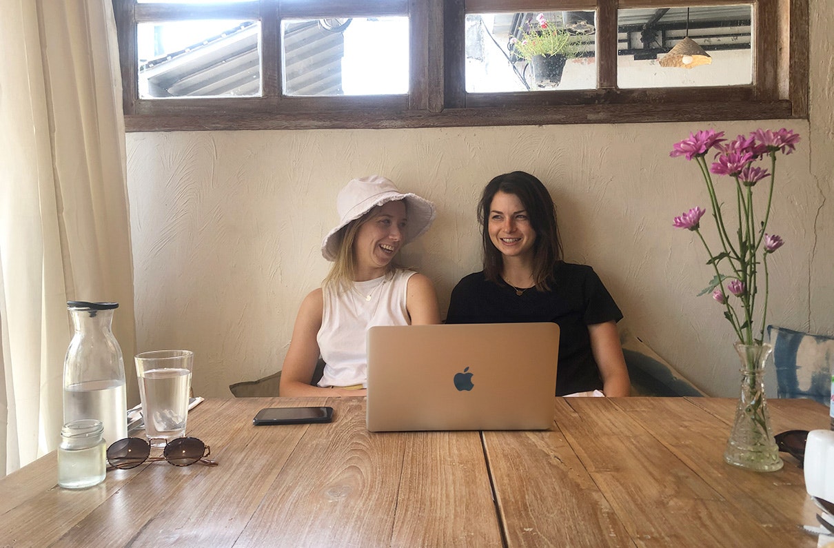 Two woman sit at a cafe table with a laptop