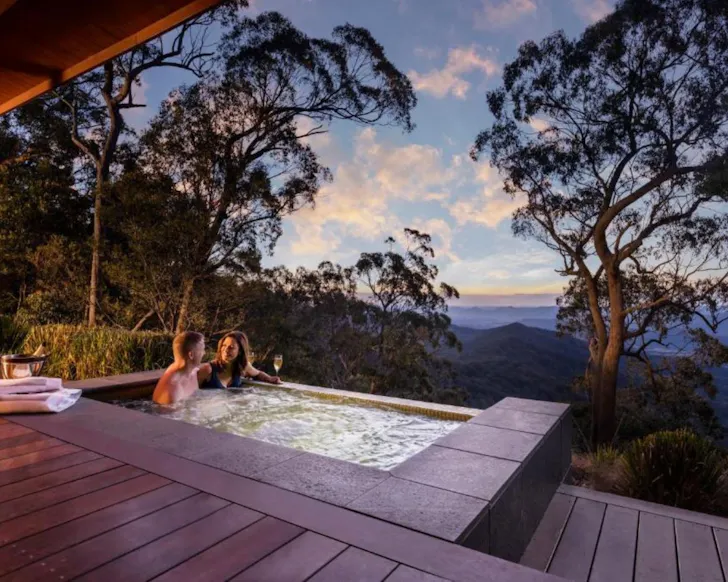 A couple bathes in the spa with champagne, looking out over the landscape at Spicers Peak Lodge one of the best romantic getaways in Australia