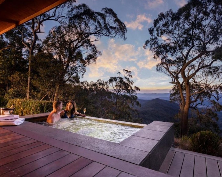 A couple bathes in the spa with champagne, looking out over the landscape at Spicers Peak Lodge one of the best romantic getaways in Australia