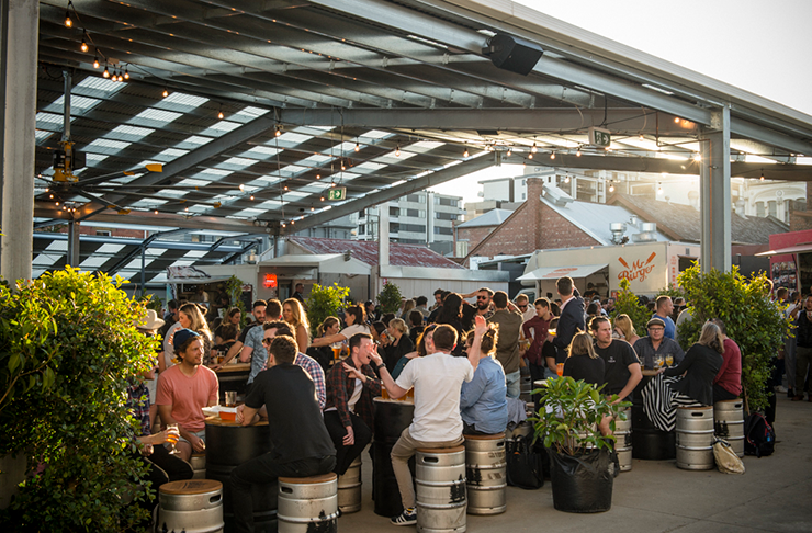 The outdoor beer area of Welcome To Brunswick with people seated at the tables drinking and talking 