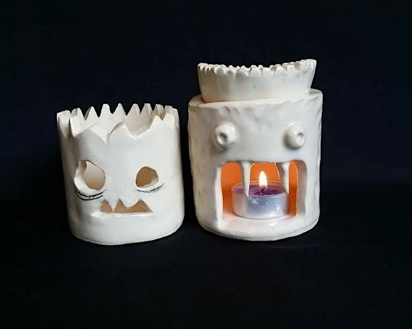 Two spooky lanterns made out of clay levitate on a black background as if by some Halloween sorcery. 
