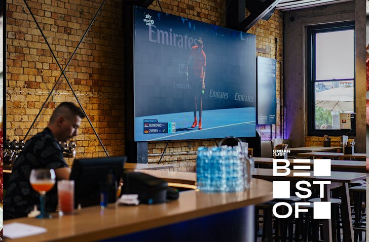 A bartender is busy behind the bar while a sports game plays on a massive screen at Tyler St Sport. 