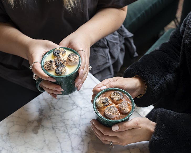 Two people hold their steaming mugs of hot chocolate.