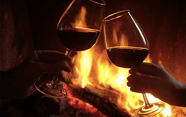 A couple cheers their red wine glasses in front of a roaring fire at Stafford Road Wine Bar.