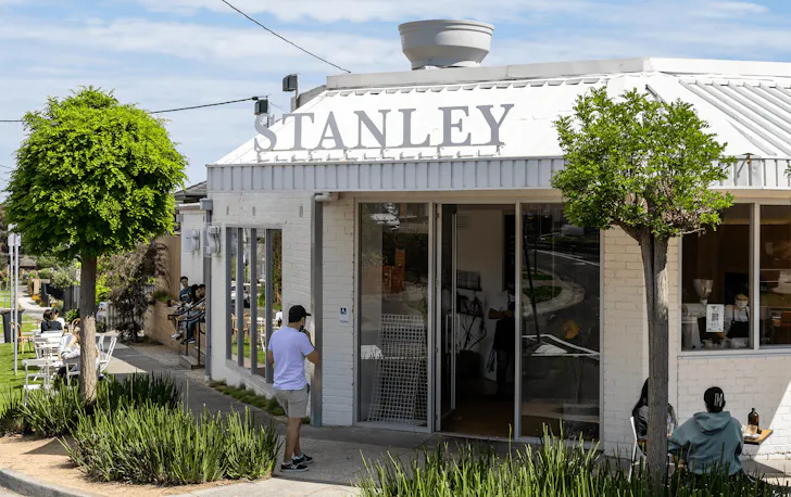A white cafe on a corner with green leafy trees out front.