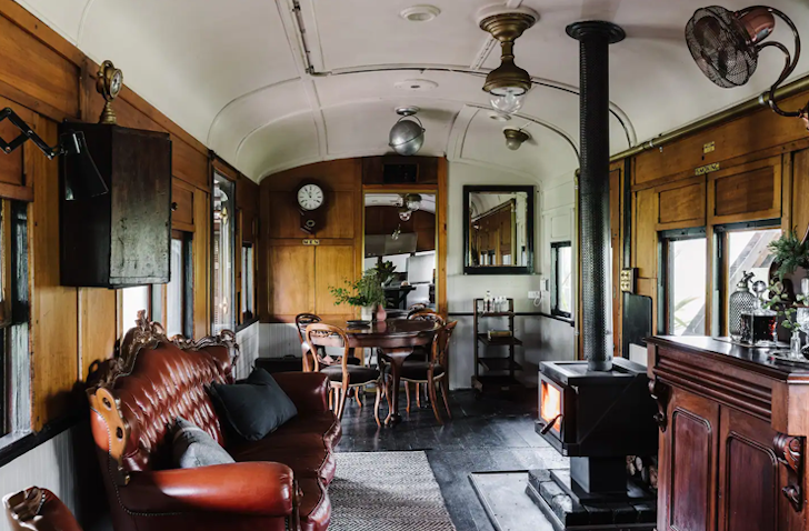 A fireplace and leather couch sits inside a tiny home that takes shape as converted vintage train carriage.