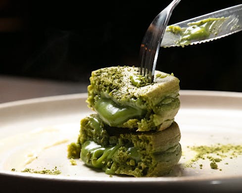 A halved, stacked pancake oozes dark green matcha cream. 