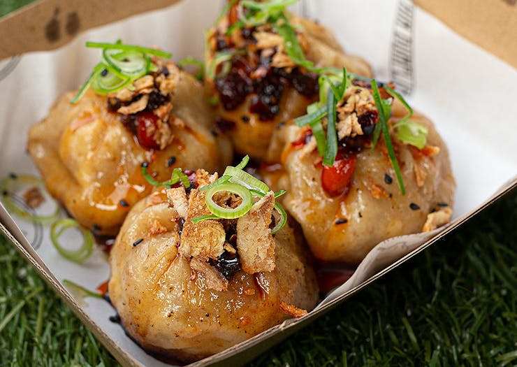 Four golden, mouth-watering  dumplings topped with spring onions and chilli sitting in a box. 