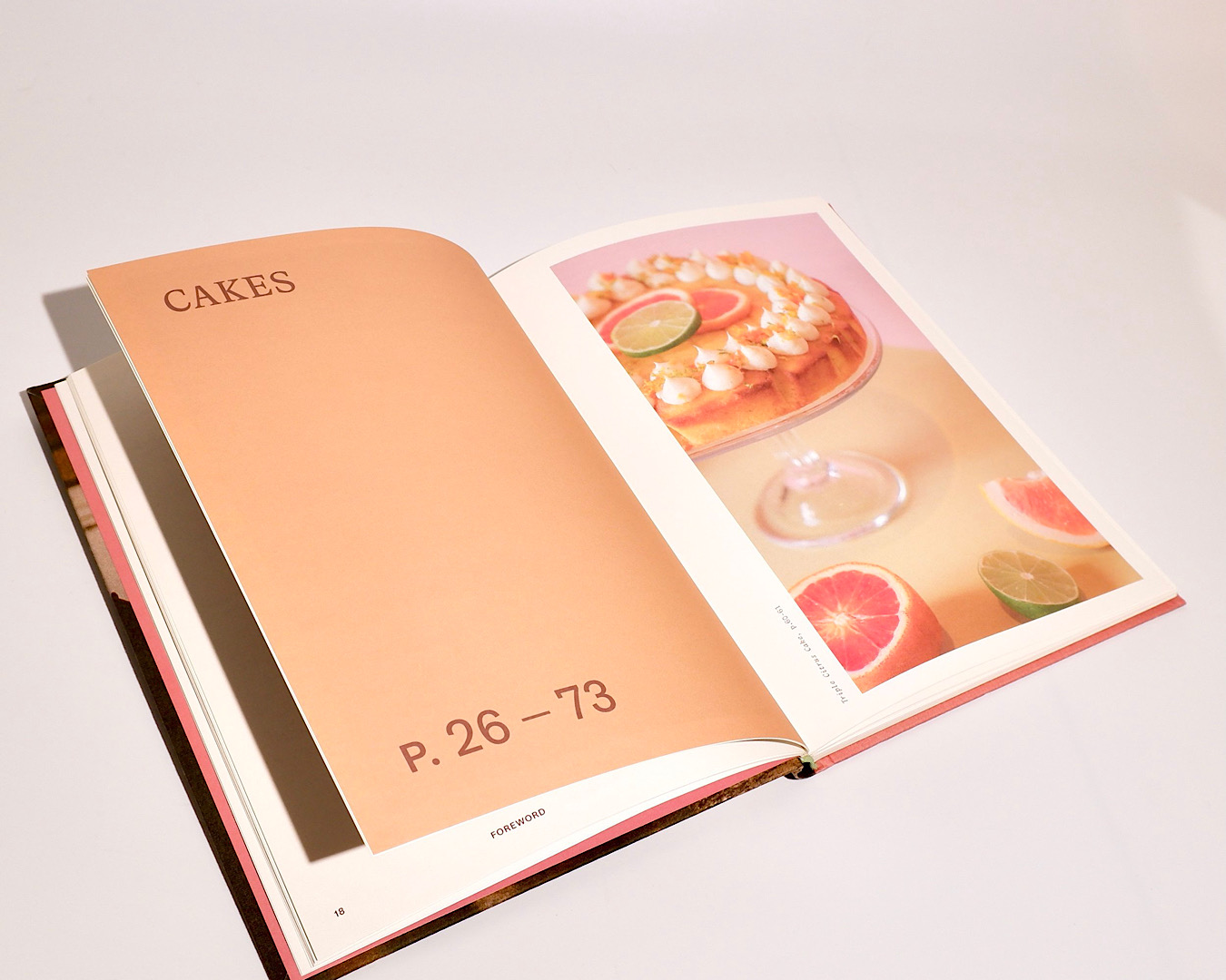 A recipe book lies open on the cakes page. Overleaf is a stunning cake topped with mini meringues and slices of citrus. 