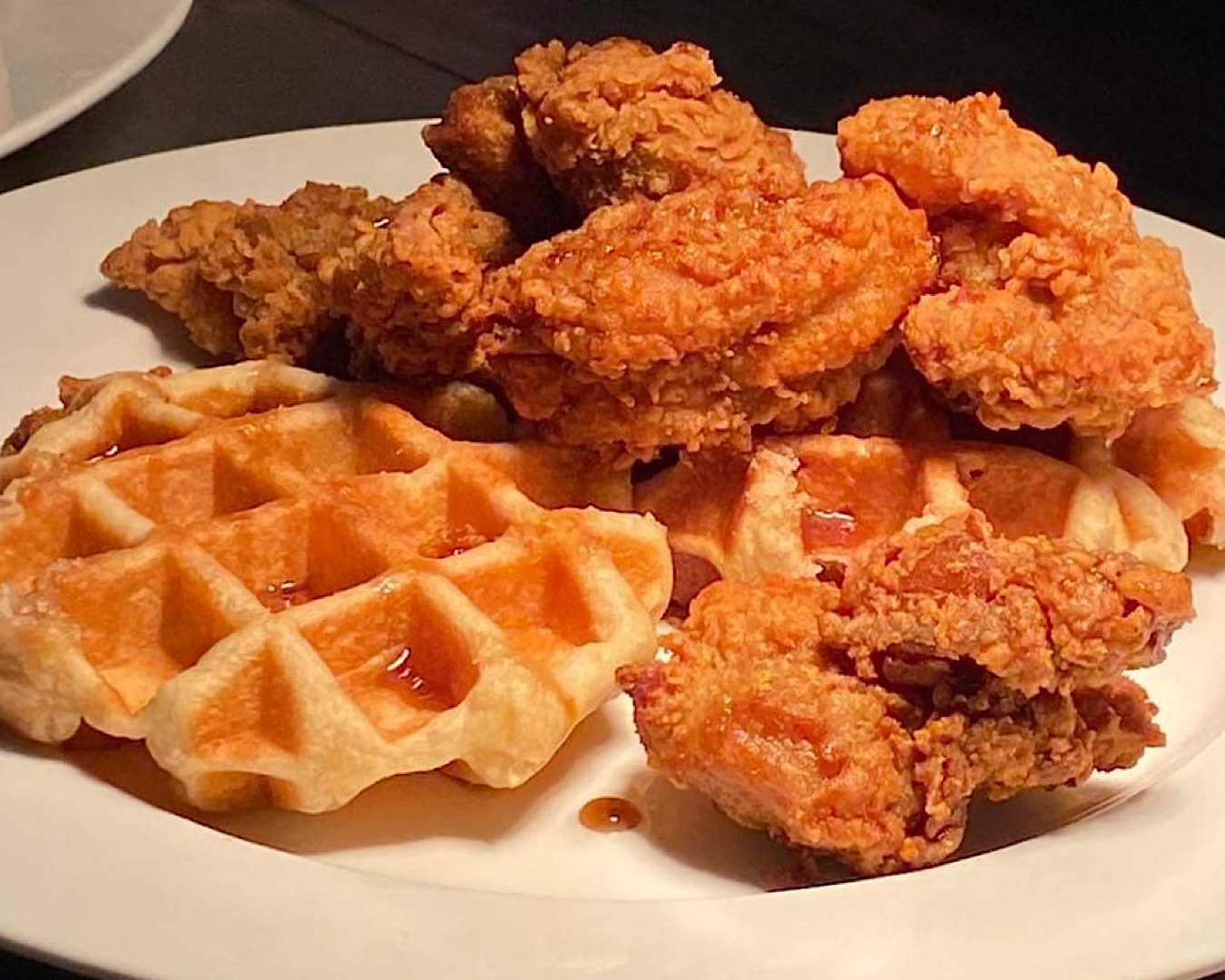 Waffles and crispy fried chicken with maple syrup on a white plate at Sweat Shop and Brew Kitchen’s bottomless fried chicken and waffles.