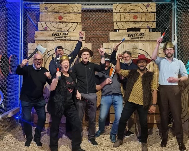 A group wearing costume hats scream at the camera and hold axes. 