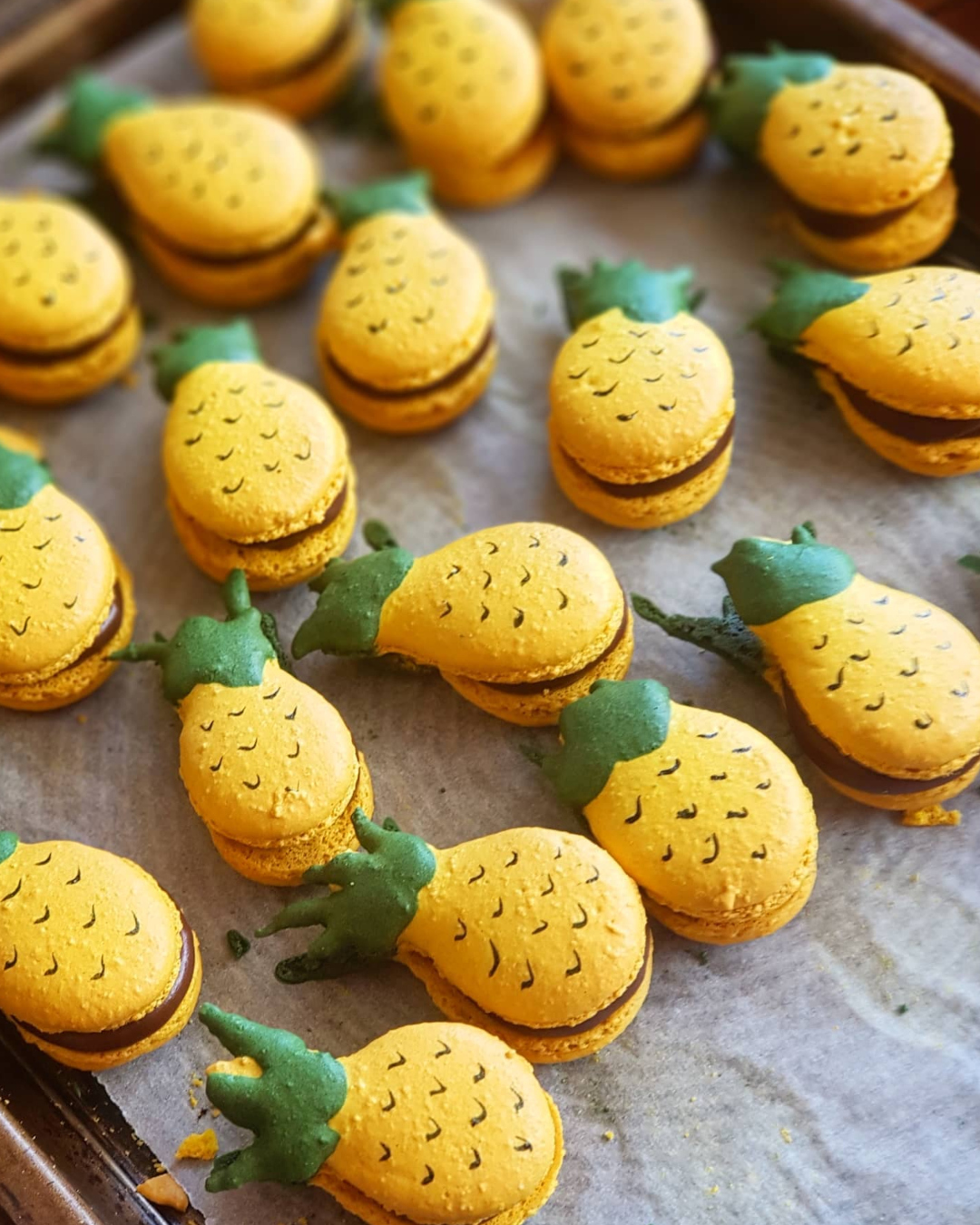 A tray of cute bright yellow and green pineapple-shaped macarons. 