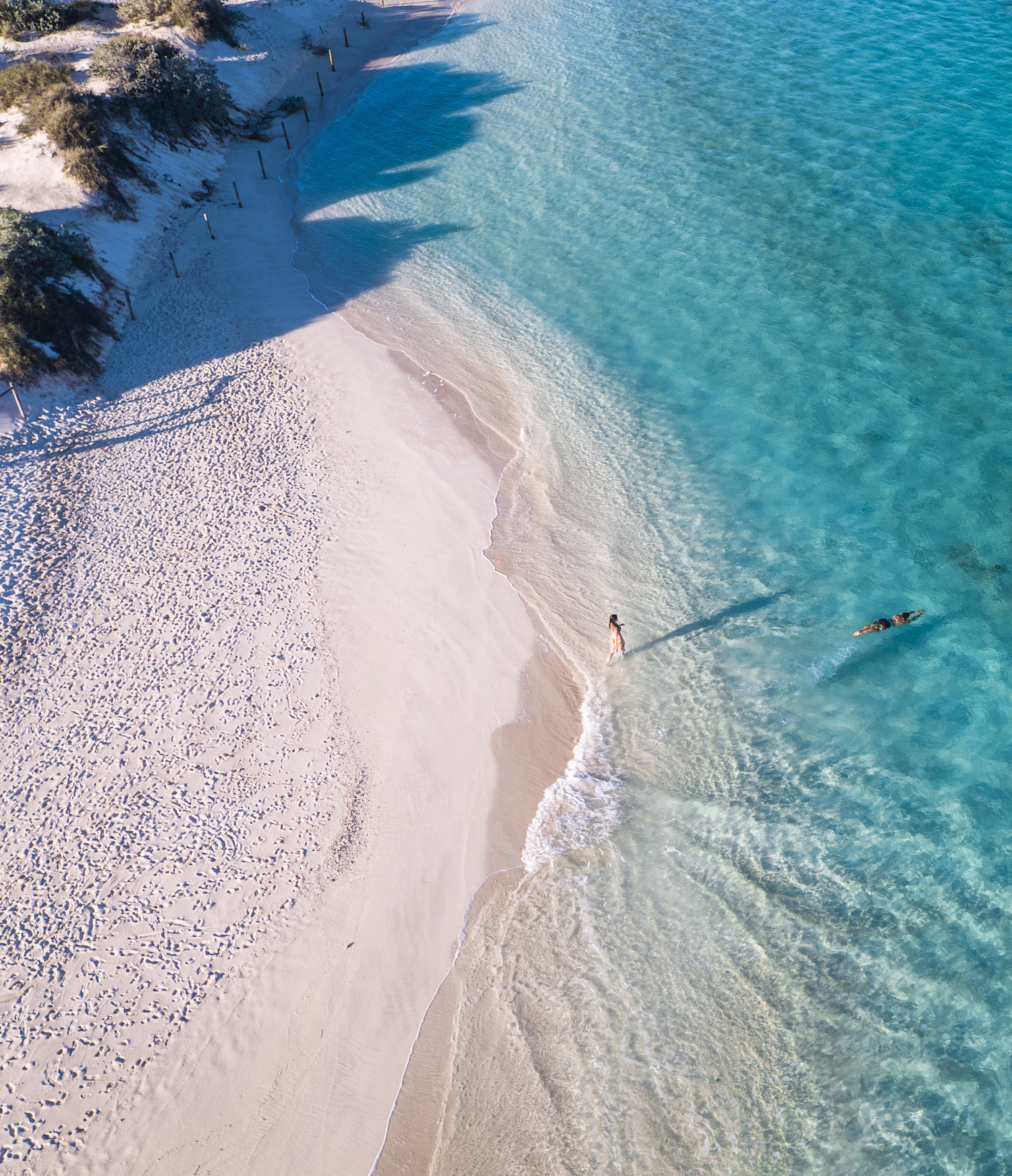 An aerial shot of two people swimming in crystal clear waters.
