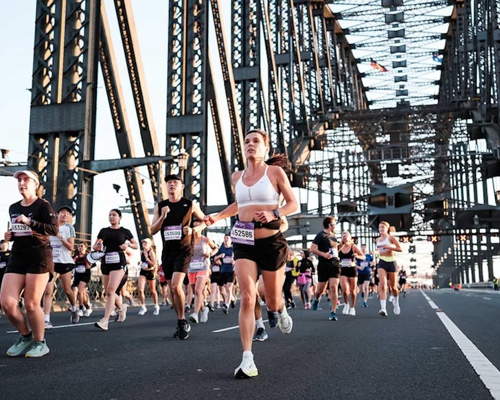 TCS Sydney Marathon 2025, A group of marathon runners crossing the Sydney Harbour Bridge. The view is a mid-shot of the runners and the Harbour Bridge's design is recognisable in the background. 