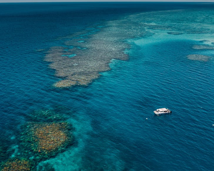 A small boat floats in the Great Barrier Reef, surrounded by heritage-listed coral gardens.