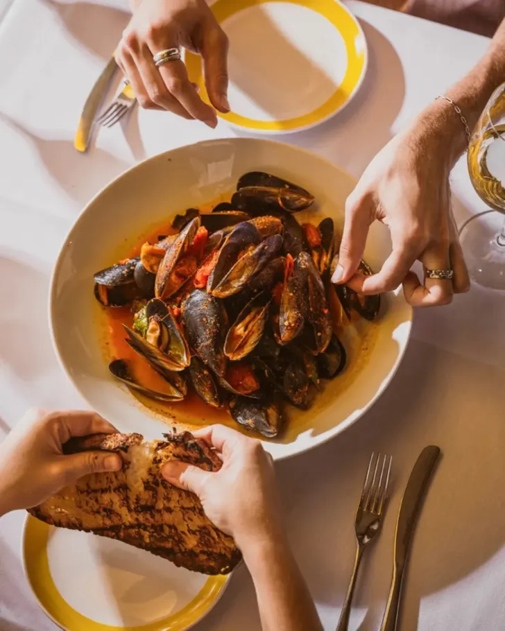 Plate of mussels with hand grabbing and hand breaking bread