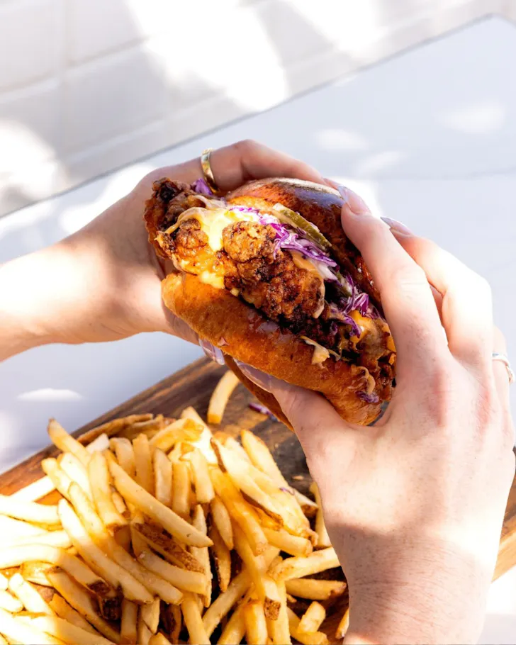Hands around stacked chicken sandwich with fries below