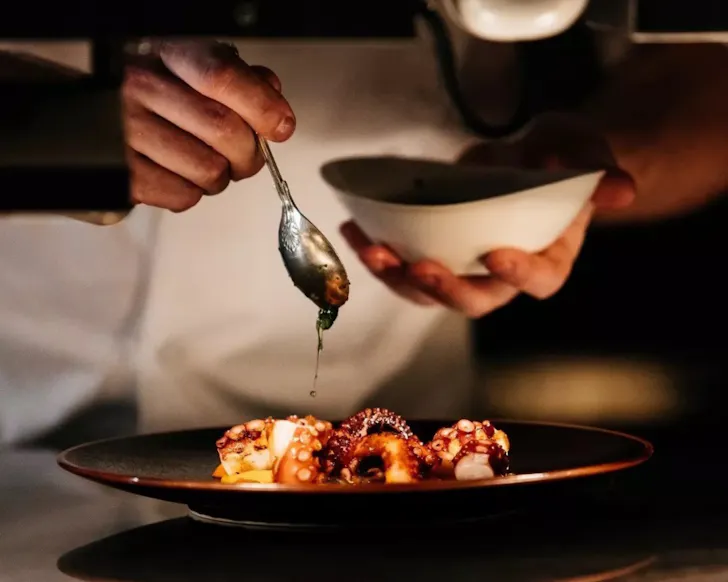 Hand holding bowl pouring orange liquid of octopus legs