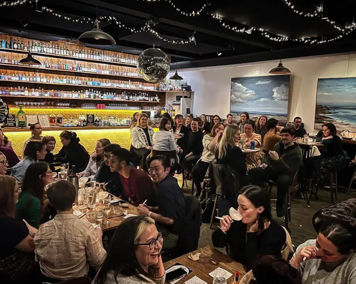 Busy venue of people sitting at tables in front of a bright bar