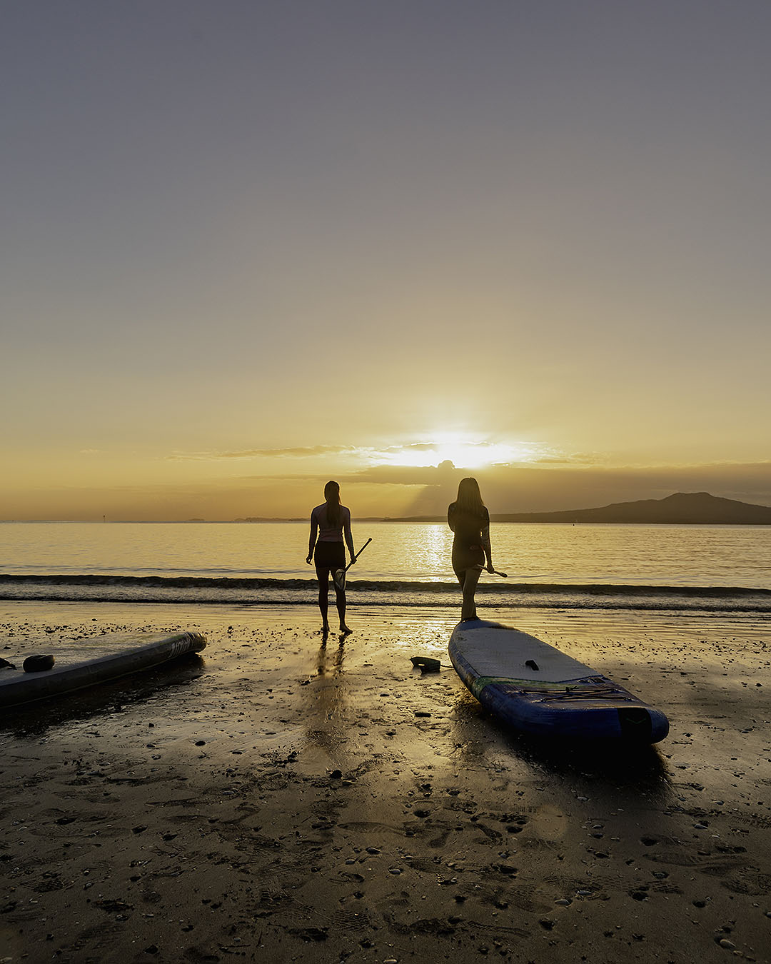 Women preparing for a morning paddle board on Takapuna Beach.