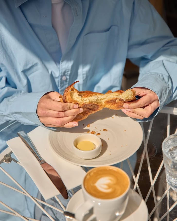 A person tucks into a croissant and coffee at Takapuna Beach Cafe. 