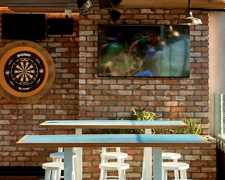 Sports on the tv, a dart board and two blue high tables at Takapuna Surf Club. 
