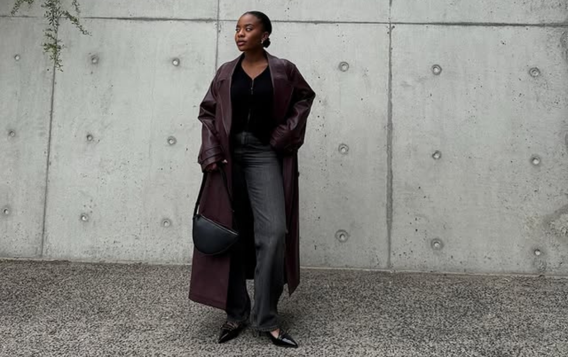 Woman dressed in black with maroon trench coat posing in front of concrete wall