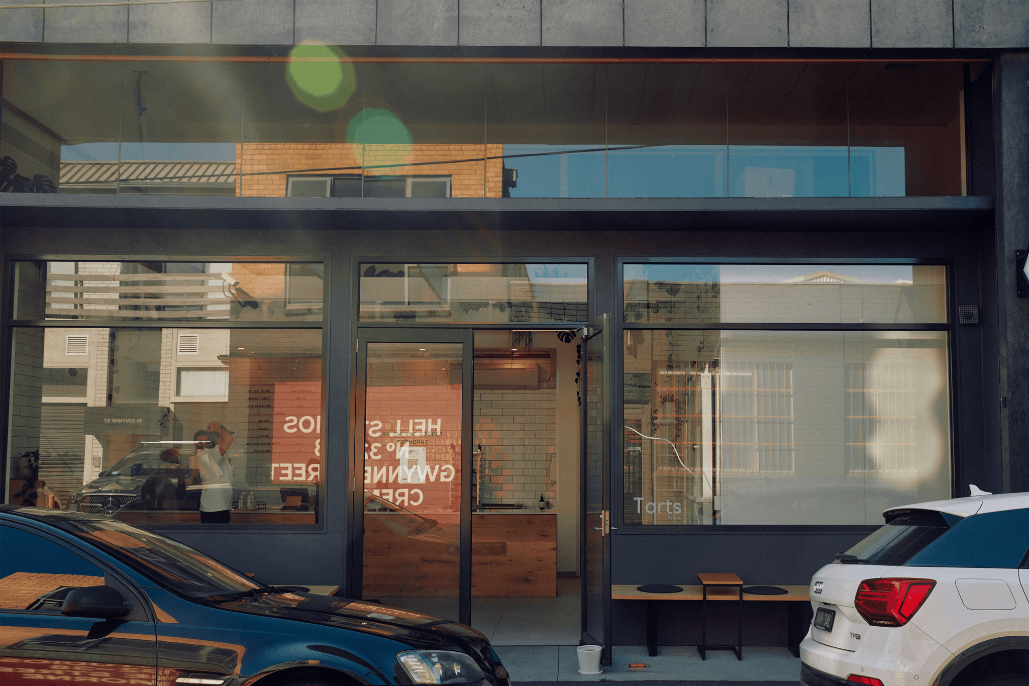 A storefront with two cars parked out in front. 