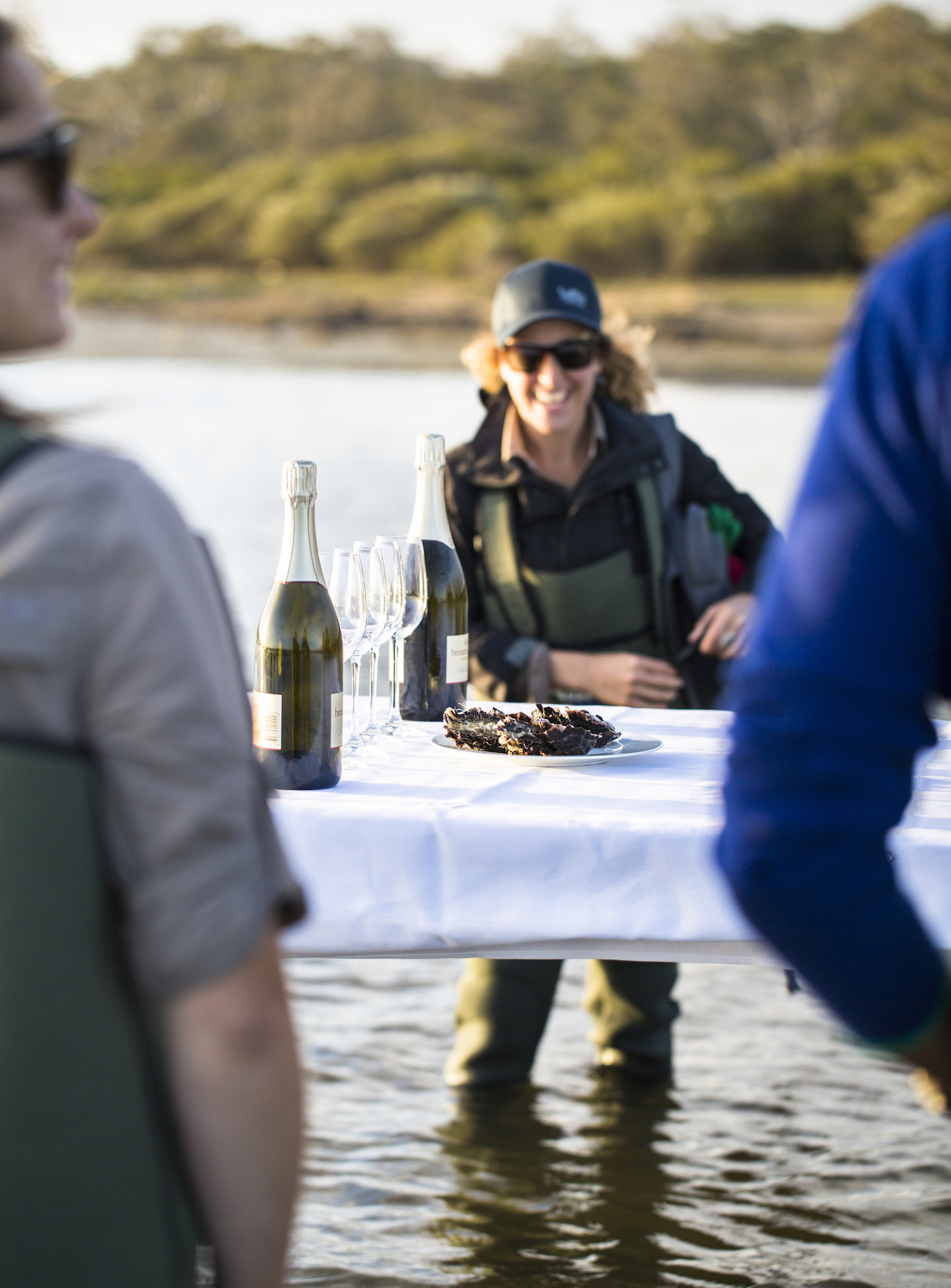 An oyster farmer wades in the water as they chat to guests.