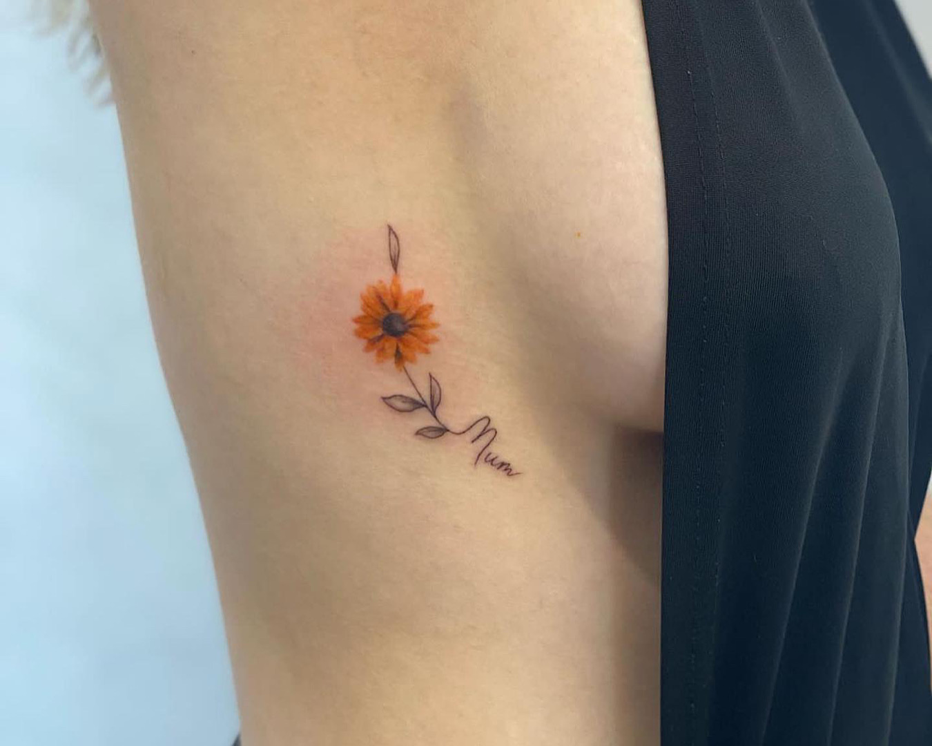 A dainty flower tattoo with the word ‘Mum’ written into the stem. Tattooed by Tattoo Gold, one of the best tattoo studios in Auckland. 