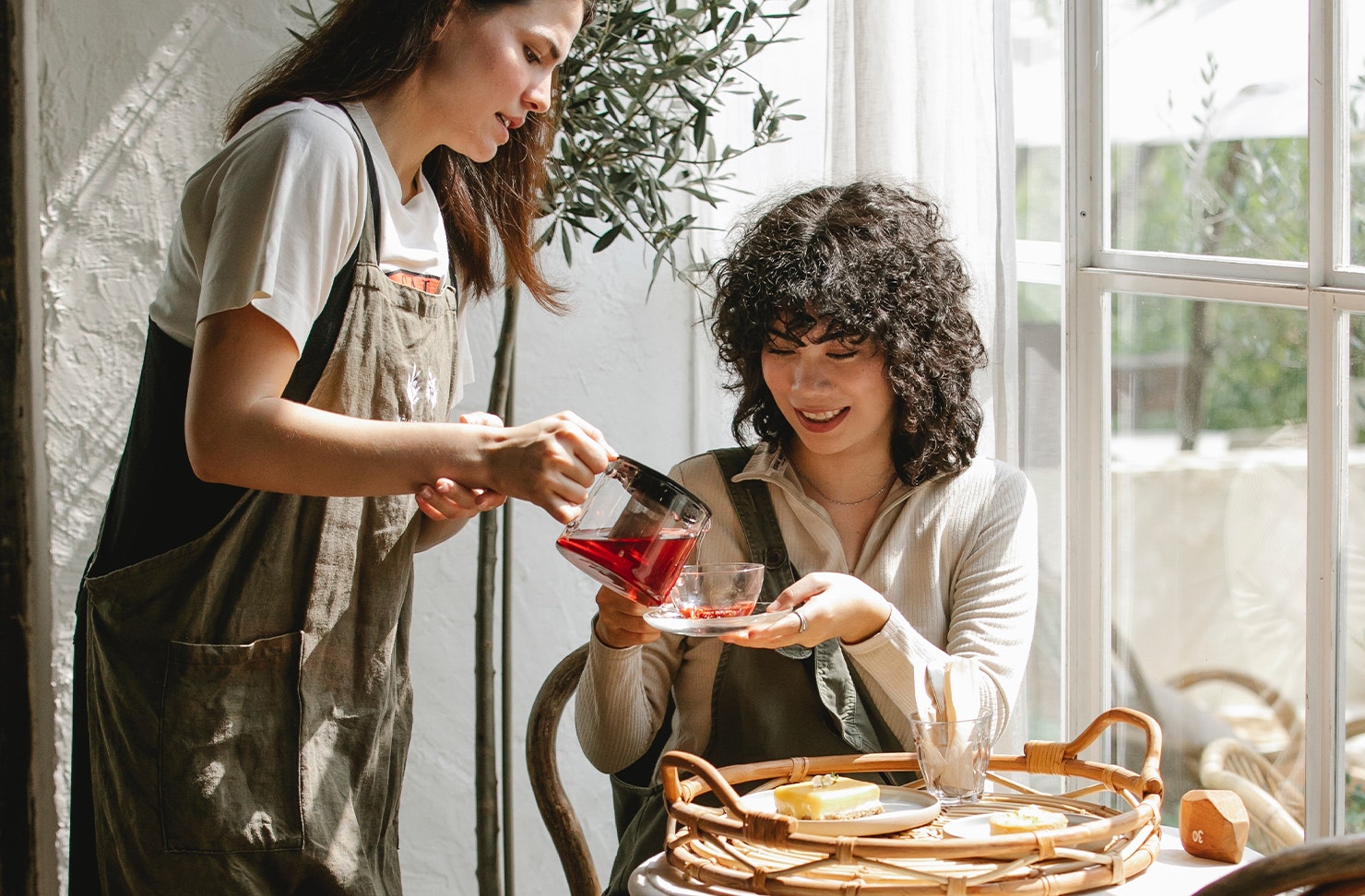 One girl pouring another crimson coloured tea. 