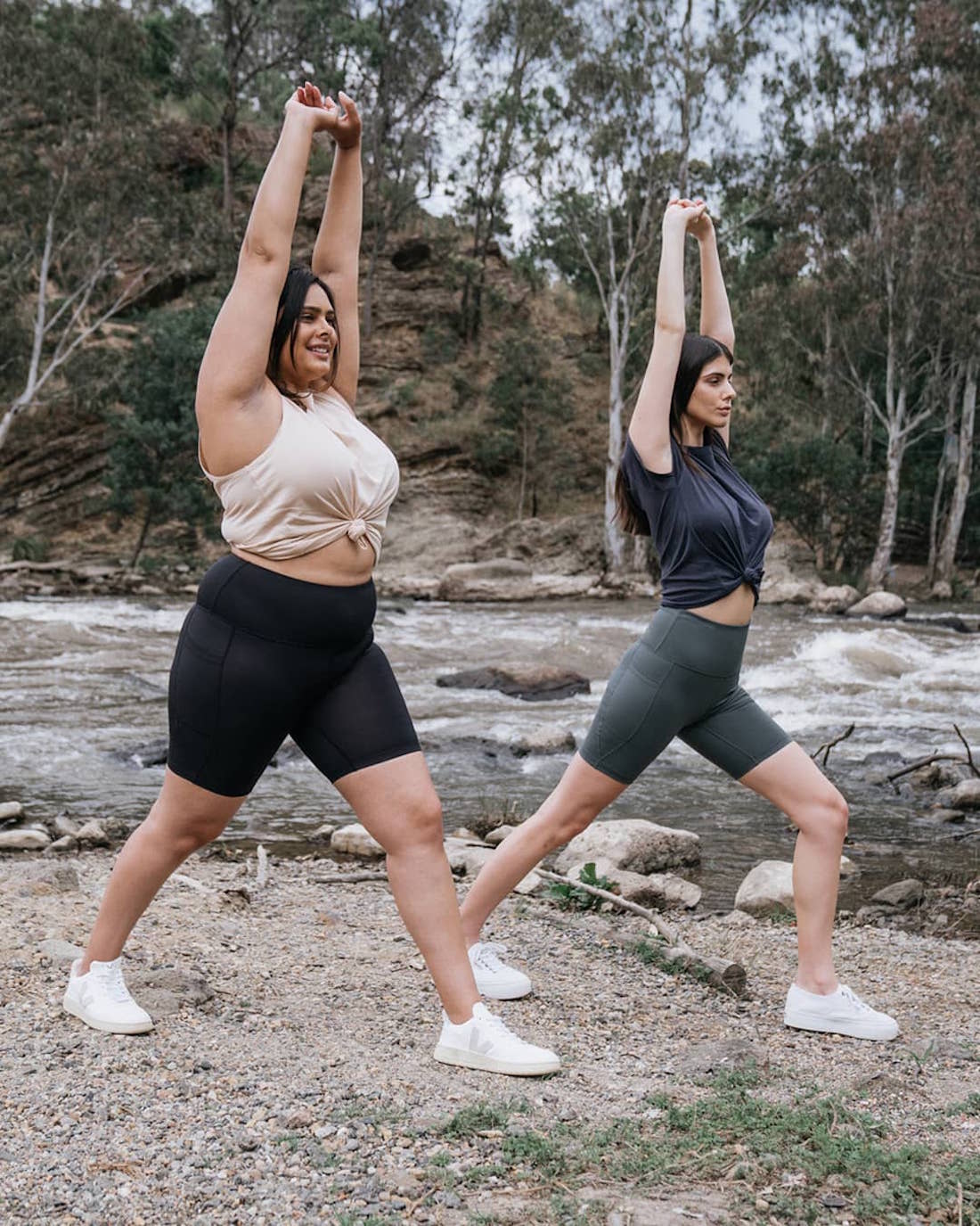 Two women stretch in the bush rocking their bike shorts.