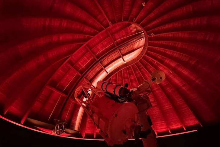 A mighty telescope commands attention, bathed in red light. 