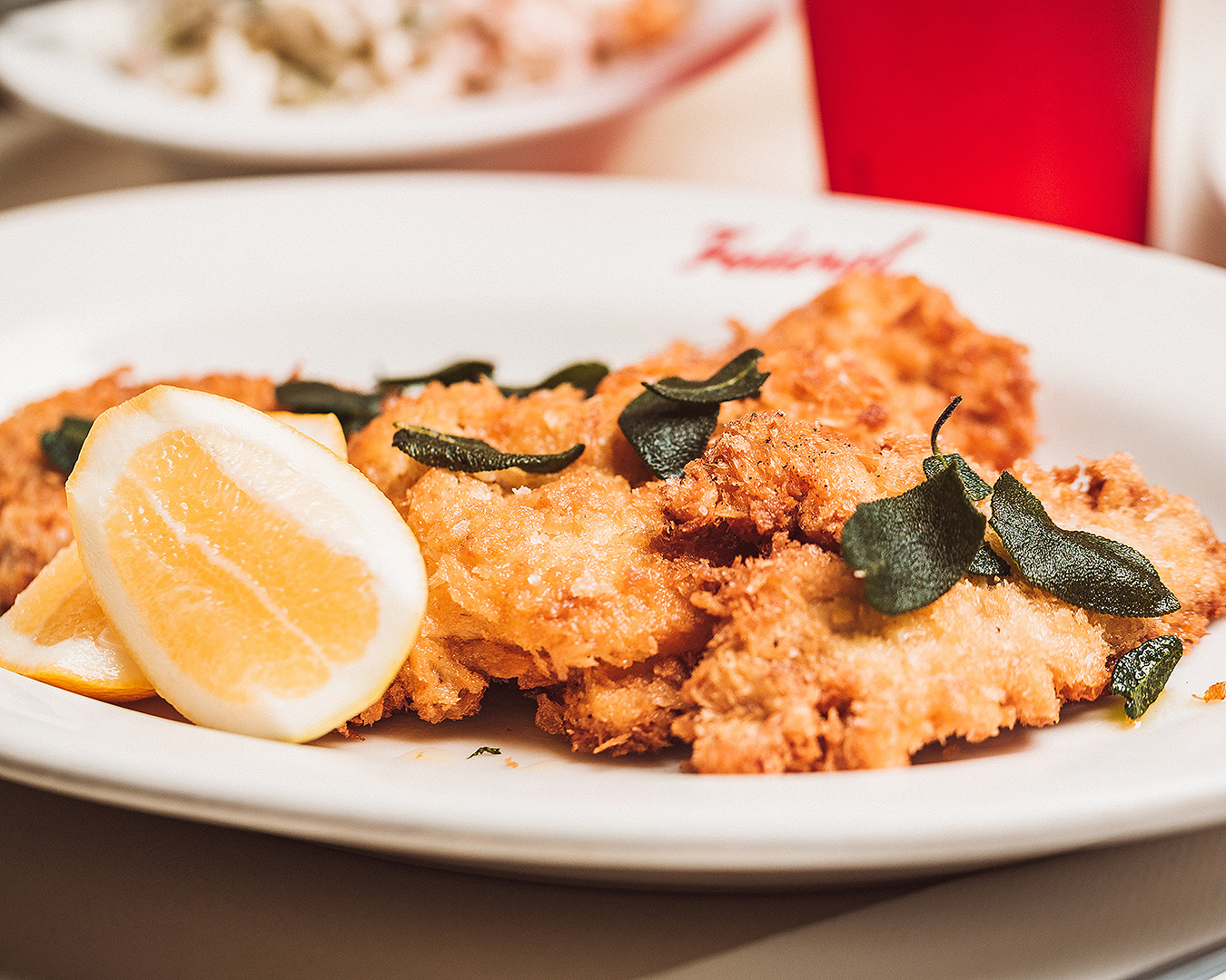 A delicious looking schnitzel from Federal Delicatessen sitting on a plate with crispy sage leaves on top and a slice of lemon. One of the best schnitzels in Auckland.