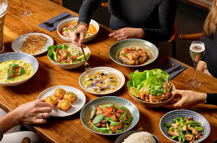Three people diving into a spread of dishes for mother's day in Melbourne including kingfish