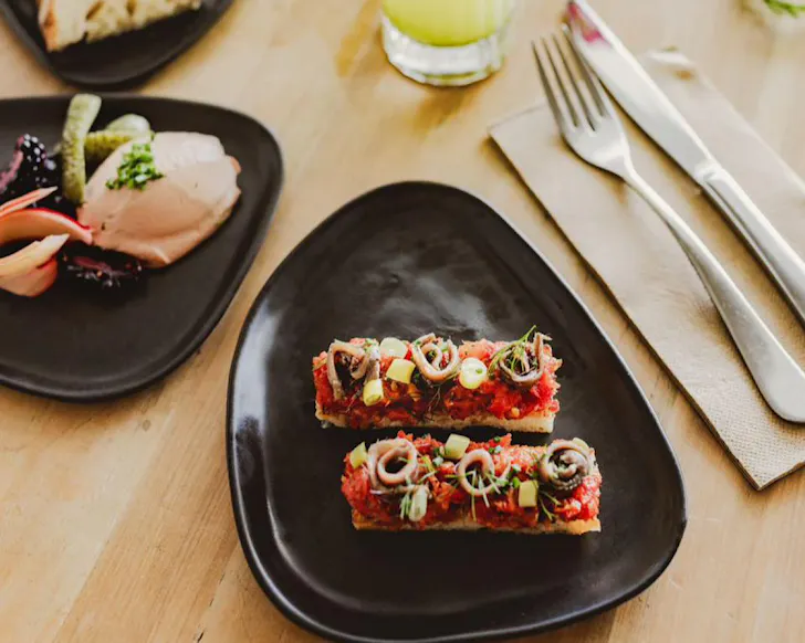 Two slices of vibrant anchovy toast on a triangular-ish shaped black plate. 