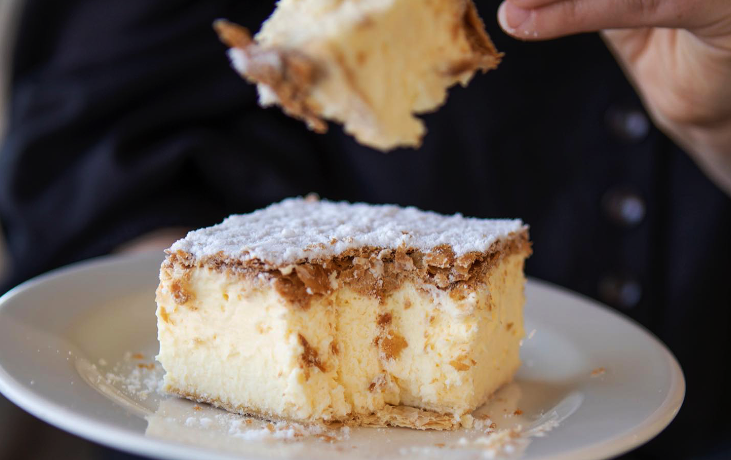 A person taking a forkful of a best vanilla slice melbourne. 