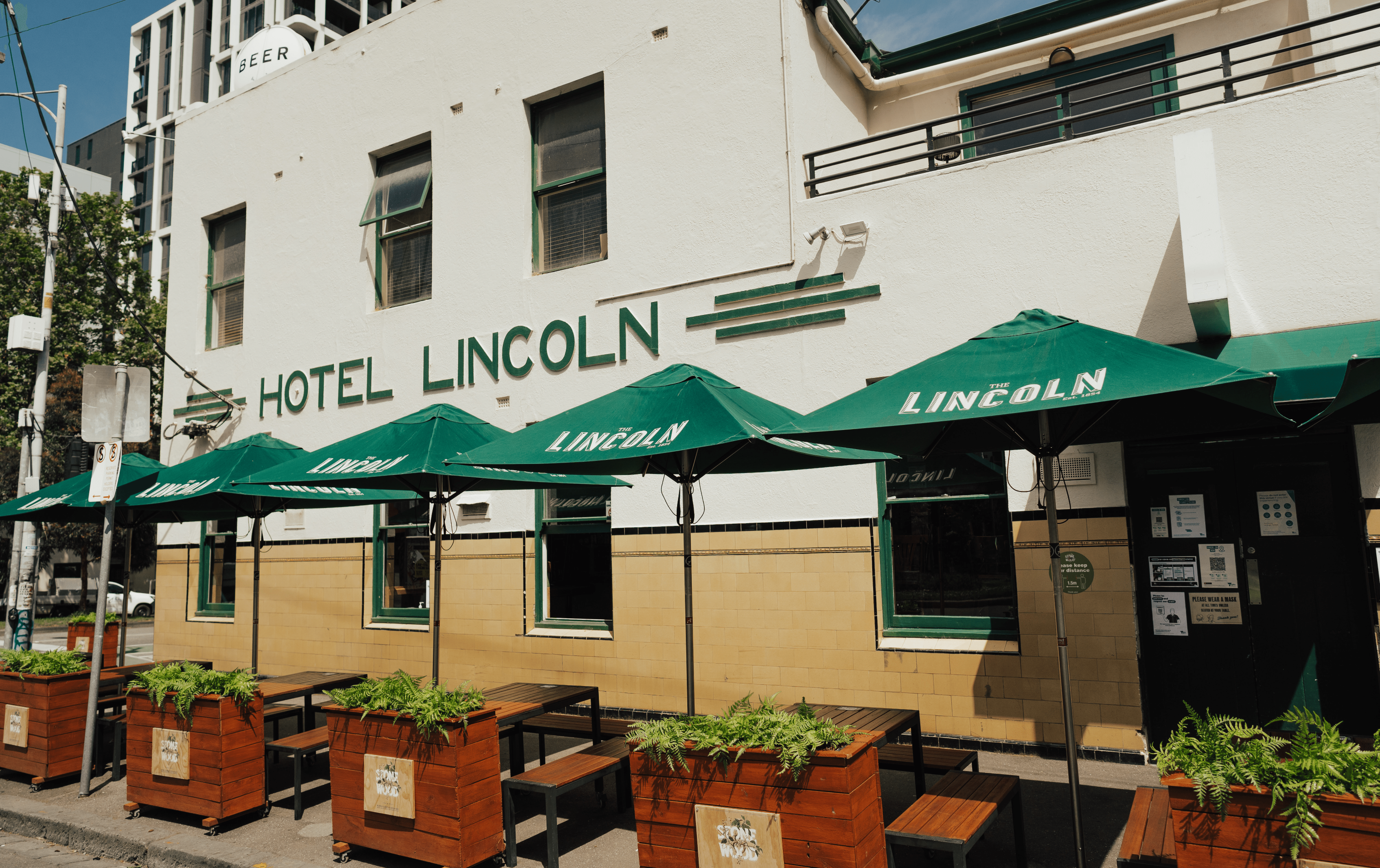 The exterior of a white building with green umbrellas outside, one of the best pubs in Melbourne.