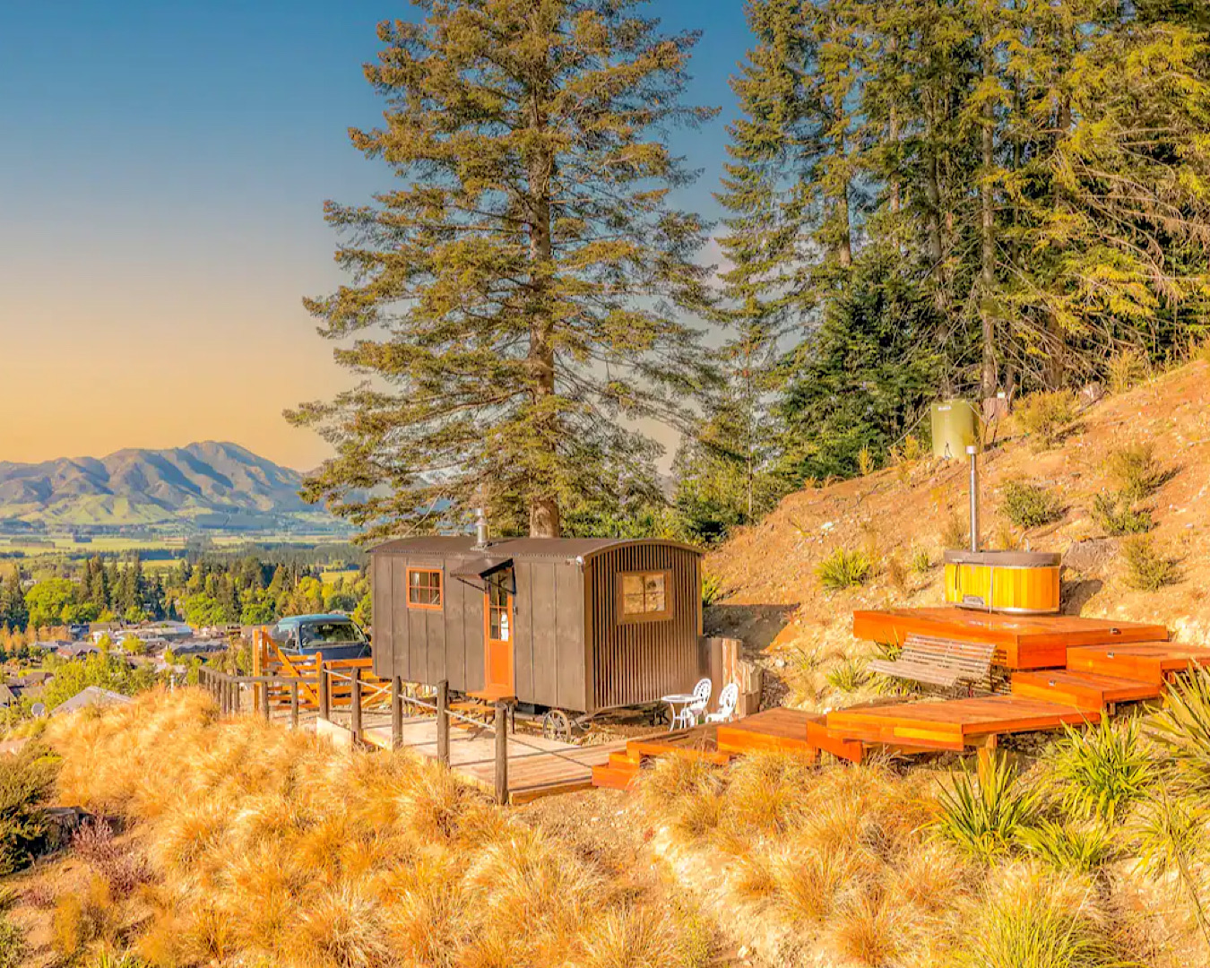 A tiny-home style brown hut with an orange door surrounded by a beautiful nature expanse and mountains at one of the best places to stay in Hanmer Springs. 