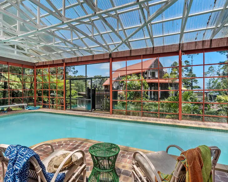 A massive swimming pool surrounded by a red structural glasshouse at The Aviary, one of the best airbnbs with a swimming pool. 